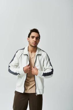 A young African American man poses in a stylish white jacket against a grey background. clipart