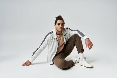 Gri bir arka planda şık giyinmiş Afrikalı Amerikalı genç bir adam poz veriyor..