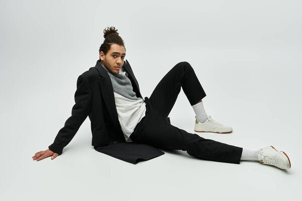 A stylish African American male model wears an elegant coat and sits on a grey background.