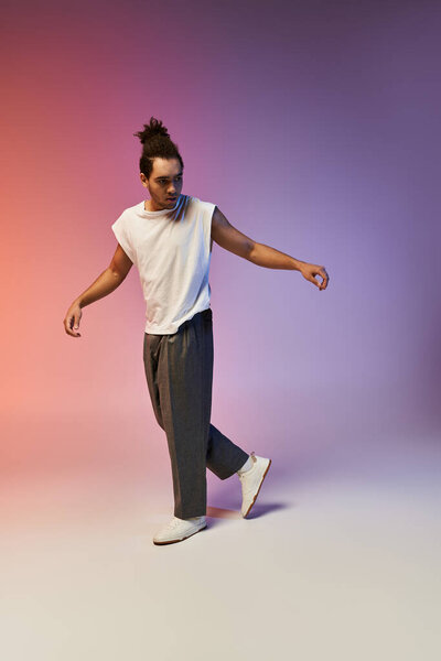 Молодой афроамериканец танцует на фоне яркого градиентного фона. На нем белая рубашка без рукавов и серые брюки..