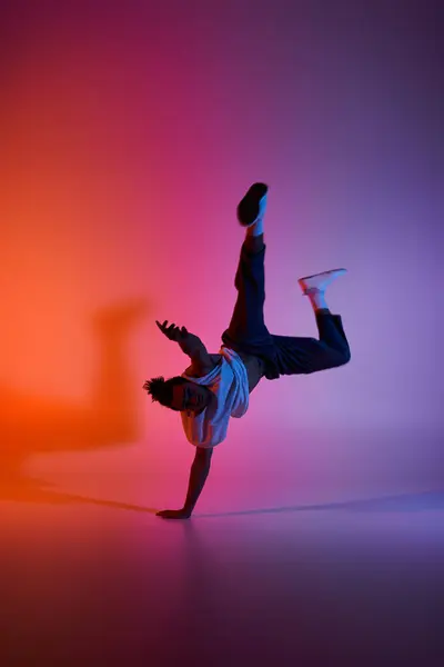 stock image A young African American man performs a dynamic dance move, silhouetted against a colorful gradient background.