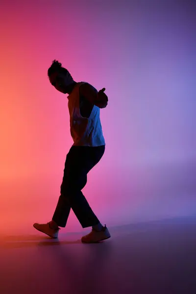 stock image A young African American man dances in a studio, his silhouette framed against a vibrant gradient background of pink and blue.