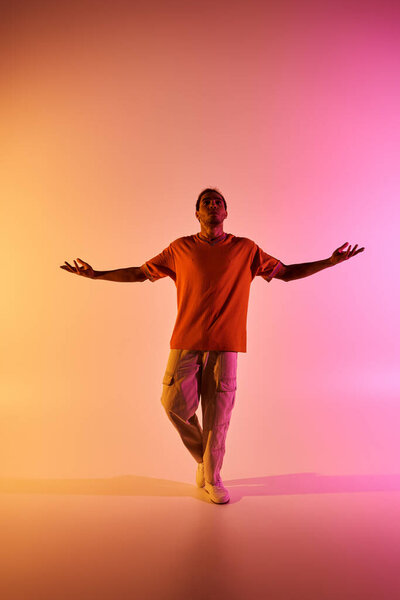 An African American male dancer poses with arms outstretched under colorful gradient lighting.