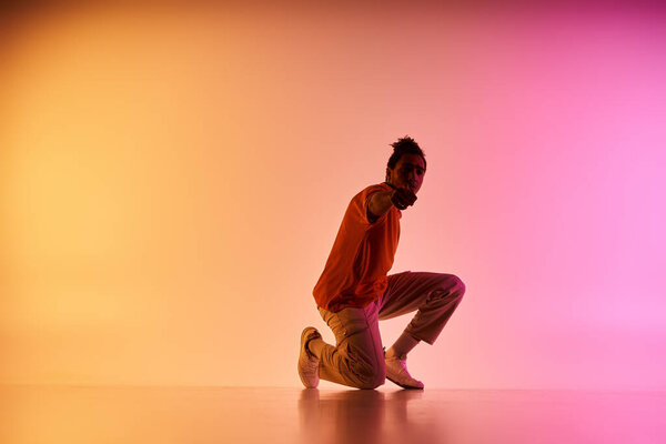 A young African American male dancer poses in a studio setting against a colorful gradient background.