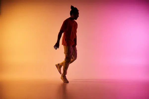 stock image A young African American man dances in front of a colorful gradient background. He is wearing a casual outfit and sneakers.