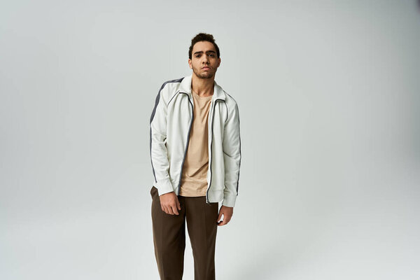 A young African American man is wearing a white jacket and posing against a grey backdrop.
