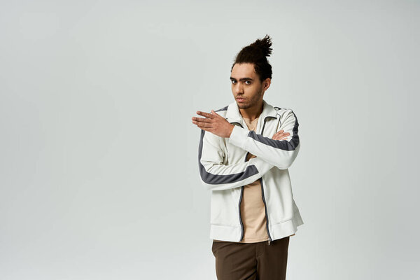 A young African American man in a stylish white jacket poses with arms crossed in front of a grey background.