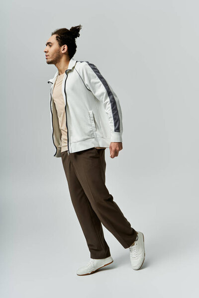 A young African American man in a stylish white jacket and brown pants poses against a grey background.