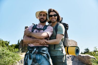 A young gay couple hikes together through nature on a sunny summer day, their smiles and embrace showcasing their love and happiness. clipart