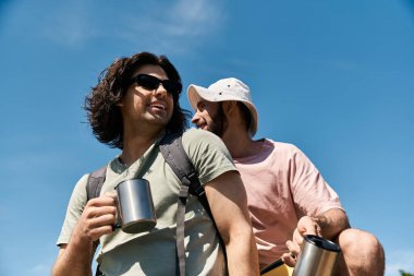 A young gay couple enjoys a hike in the wilderness during a sunny summer day. clipart