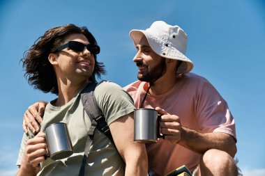 A young gay couple smiles as they hike through the wilderness on a sunny summer day. clipart