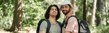 Two young men hike through a lush green forest on a summer day. clipart