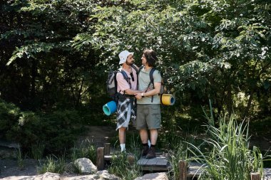 A young gay couple hikes through a lush forest in the summertime. clipart