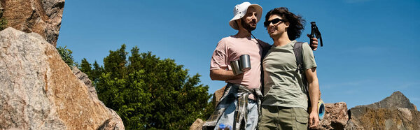 A young gay couple enjoys a summer hike in the mountains, their love evident as they share a moment in the wilderness.