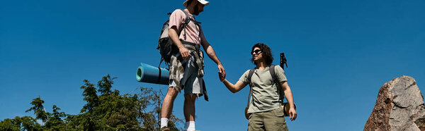 A young gay couple hikes together in a sunny, outdoor wilderness setting.
