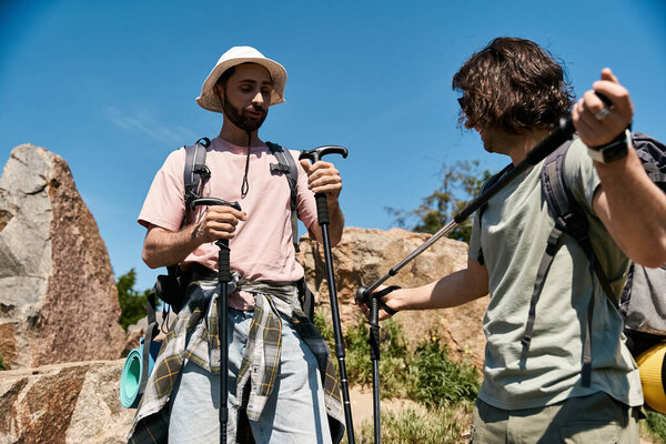 Two young men, a gay couple, hiking together in a rocky, mountainous landscape during a sunny summer day.