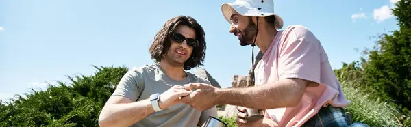 stock image Two young men, a gay couple, hike through a natural landscape on a sunny summer day.