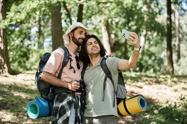 Stock image A young gay couple hikes through a lush summer forest, taking a selfie with a phone.