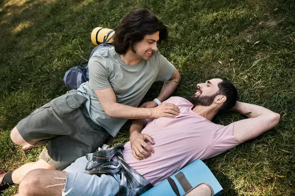 stock image Two young men, a gay couple, enjoy a summer hike, laying on the grass and smiling at each other.