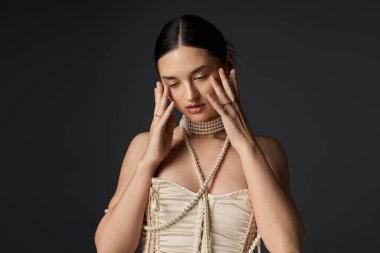 Siyah saçlı genç bir kadın, siyah bir arka fonda poz veriyor. İnci kolyeler ve zarif mücevherler takıyor. Çok güzel ve zarif..