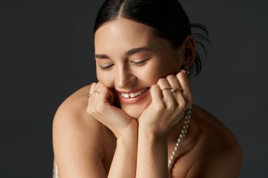 A young woman with brunette hair smiles brightly, her face adorned with delicate jewelry against a dark background. clipart