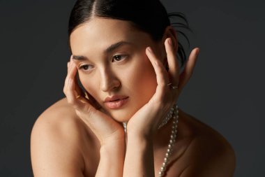 A young woman with dark hair poses against a dark backdrop, adorned with a pearl necklace. clipart