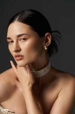 A young woman with brunette hair wears a pearl necklace and earrings against a dark background. clipart