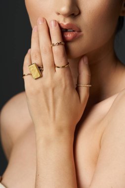 A young woman with dark hair shows off her golden rings on her fingers against a dark background. clipart