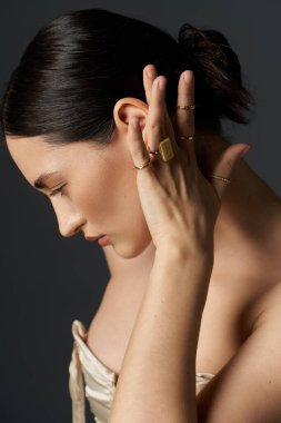 A young woman with brunette hair showcases her golden rings against a dark backdrop, highlighting the elegance and beauty of jewelry. clipart