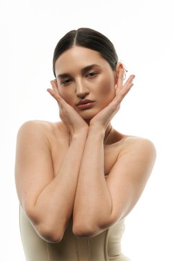 Güzel bir esmer model, elleri yüzünde dinlenirken beyaz arka planda zarif mücevherler sergiliyor..