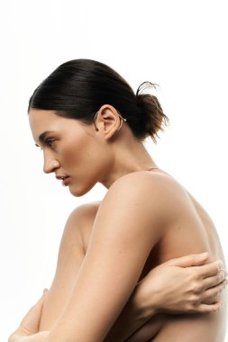 A young brunette woman with her hair pulled back displays a beautiful piece of jewelry on her ear against a white backdrop. clipart