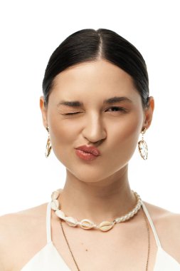 A young woman with dark hair winks playfully while showcasing a beautiful seashell necklace and earrings against a white background. clipart