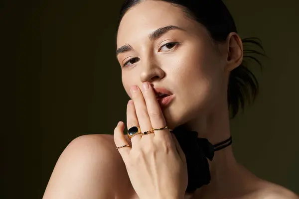 stock image A young woman with brunette hair poses against a black backdrop, adorned with a flower choker and gold rings.