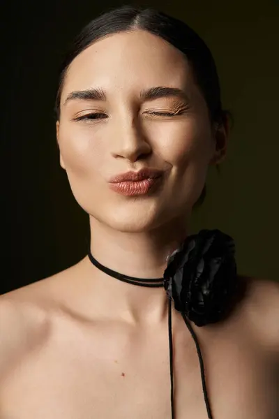 stock image A young woman with dark hair and a flower choker necklace poses with a wink and a playful smile against a black background.