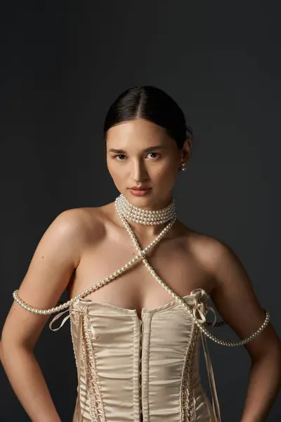 stock image A young woman with dark hair and a pearl necklace poses against a dark background.