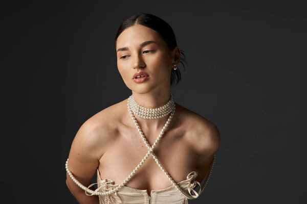 Молодая женщина с брюнетками позирует на тёмном фоне в жемчужном ожерелье.