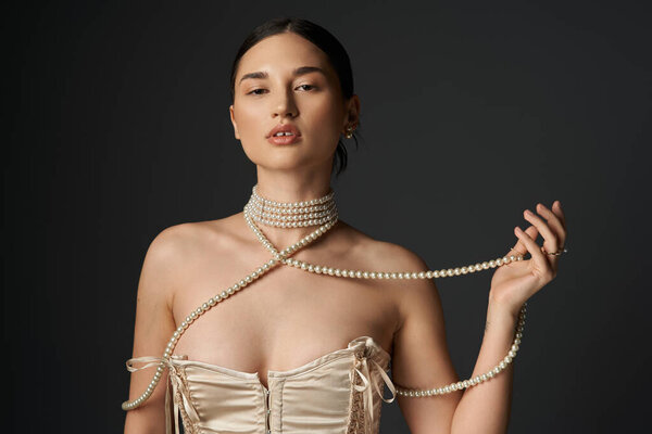 Молодая женщина с брюнетками носит жемчужное ожерелье на тёмном фоне.