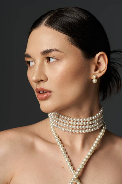 Молодая женщина с брюнетками носит жемчужное ожерелье и серьги на тёмном фоне.