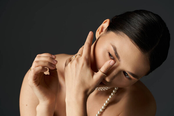 A young woman with brunette hair and a pearl necklace poses against a dark background.