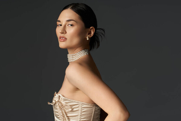 Молодая женщина с брюнетками и жемчужным ожерельем, сфотографирована на тёмном фоне.