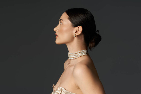 Потрясающая молодая женщина с темными волосами элегантно позирует, украшенная жемчужным ожерельем на темном фоне.