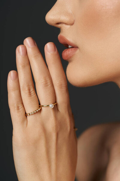 A womans hand with delicate gold rings featuring a pearl, shown against a dark background.