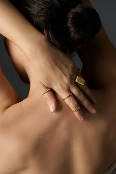 stock image A young womans hand with delicate gold rings rests against her back, creating an elegant image of beauty.