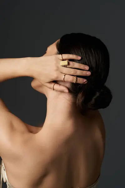 stock image A young woman with brunette hair is shown from the back, showcasing her golden rings on her fingers against a dark background.