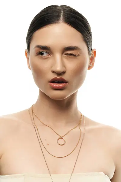 stock image A young woman with dark hair winks playfully, showcasing her beautiful, layered necklaces.