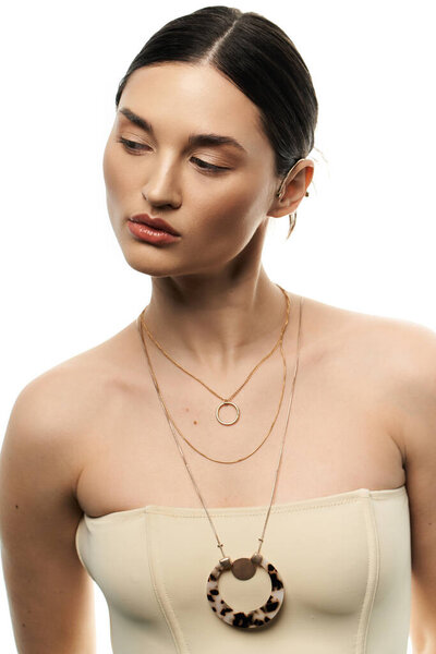 A young woman wearing a beautiful, layered gold necklace with a large tortoise pendant on a white background.