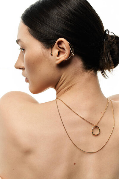 Молодая брюнетка демонстрирует нежное золотое ожерелье и наручники на белом фоне..