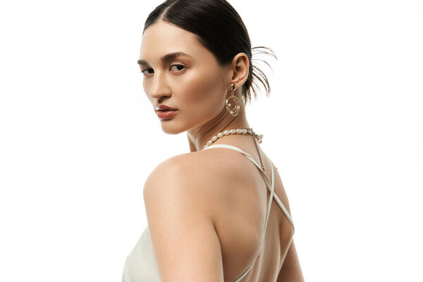 Молодая брюнетка с элегантными ювелирными изделиями позирует на белом фоне.