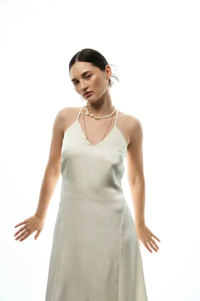 stock image A young woman with dark hair models luxurious jewelry while wearing a white dress, showcasing elegance and style.