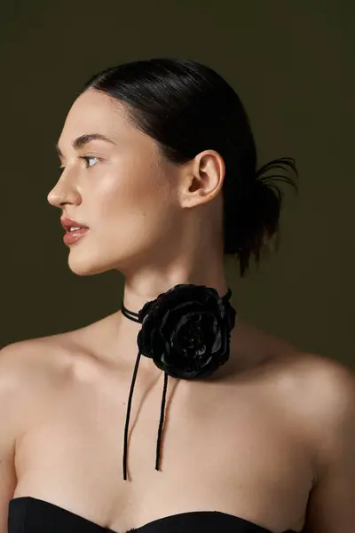 stock image A young woman with brunette hair and a black rose choker poses against a black background.